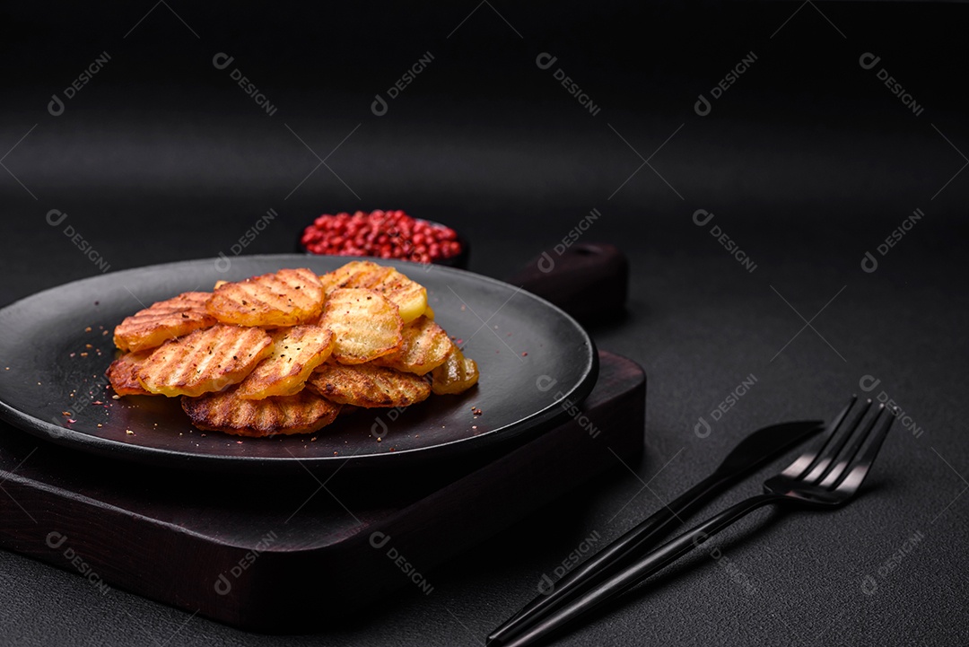 Deliciosas batatas fritas crocantes em fatias em uma placa de cerâmica preta sobre um fundo escuro de concreto