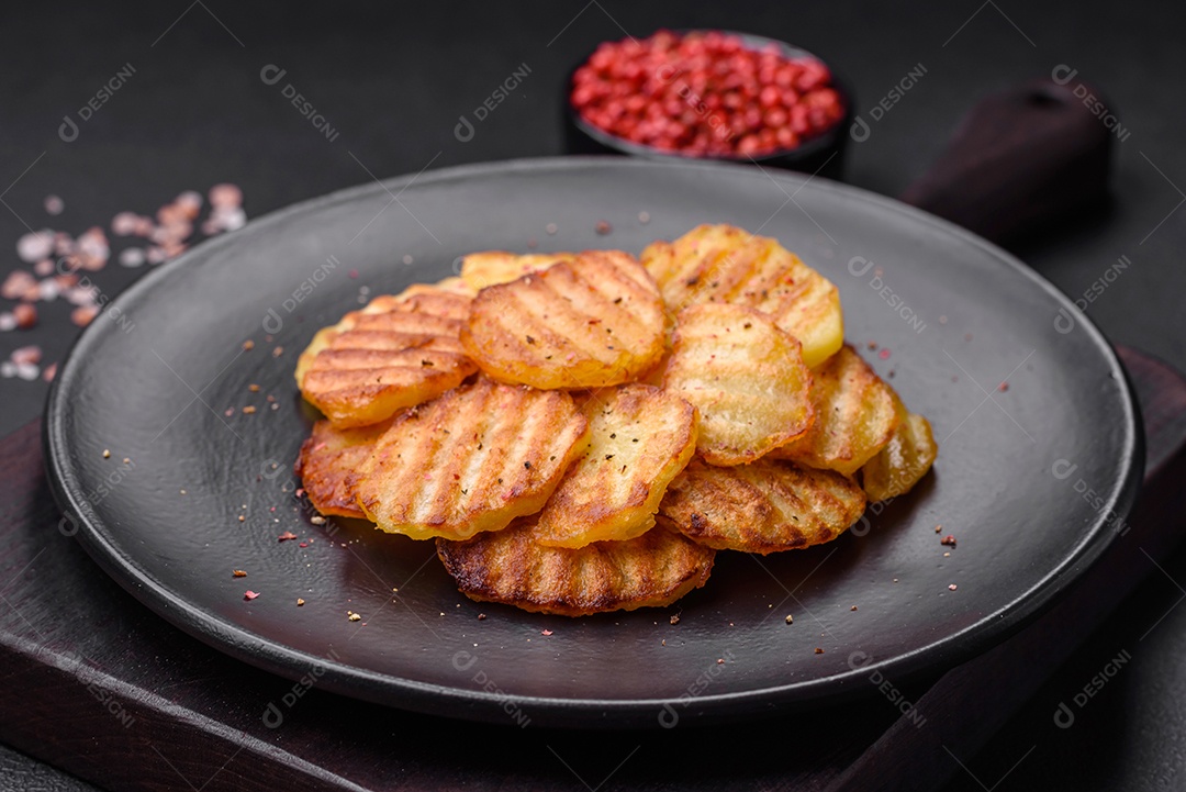 Deliciosas batatas fritas crocantes em fatias em uma placa de cerâmica preta sobre um fundo escuro de concreto