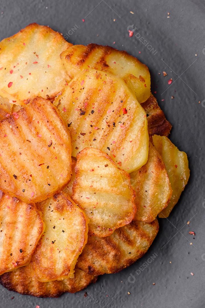 Deliciosas batatas fritas crocantes em fatias em uma placa de cerâmica preta sobre um fundo escuro de concreto