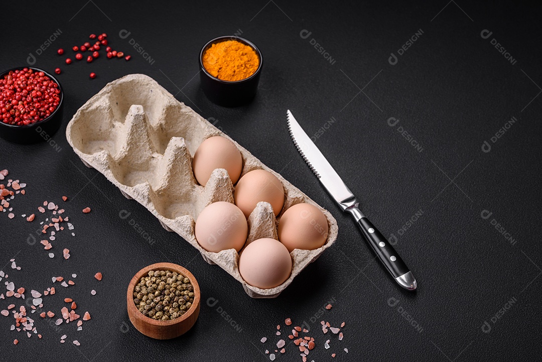 Ovos de galinha crus frescos na cor bege em uma bandeja de papelão sobre um fundo escuro de concreto