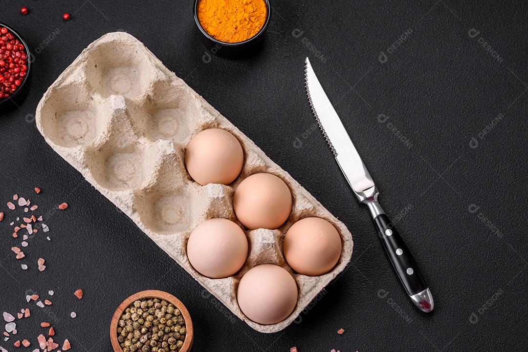 Ovos de galinha crus frescos na cor bege em uma bandeja de papelão sobre um fundo escuro de concreto