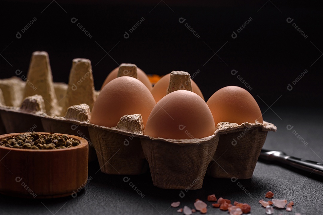 Ovos de galinha crus frescos na cor bege em uma bandeja de papelão sobre um fundo escuro de concreto