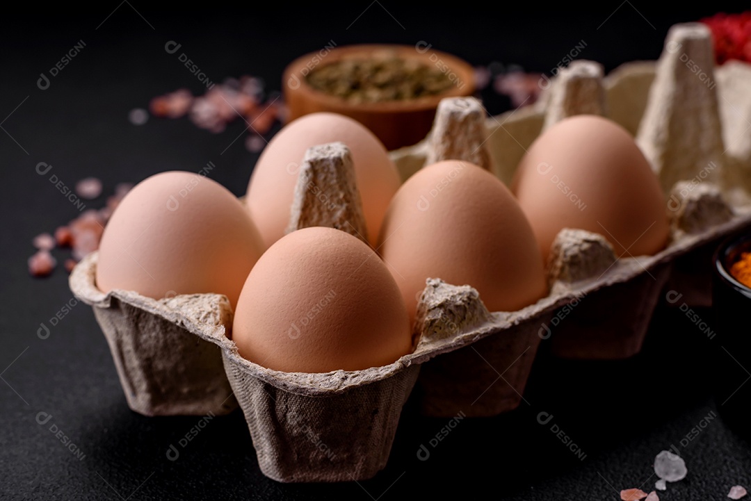 Ovos de galinha crus frescos na cor bege em uma bandeja de papelão sobre um fundo escuro de concreto