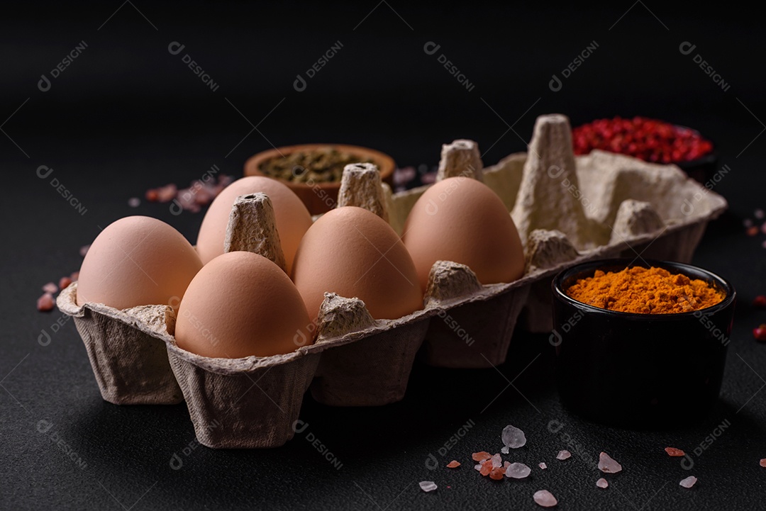 Ovos de galinha crus frescos na cor bege em uma bandeja de papelão sobre um fundo escuro de concreto