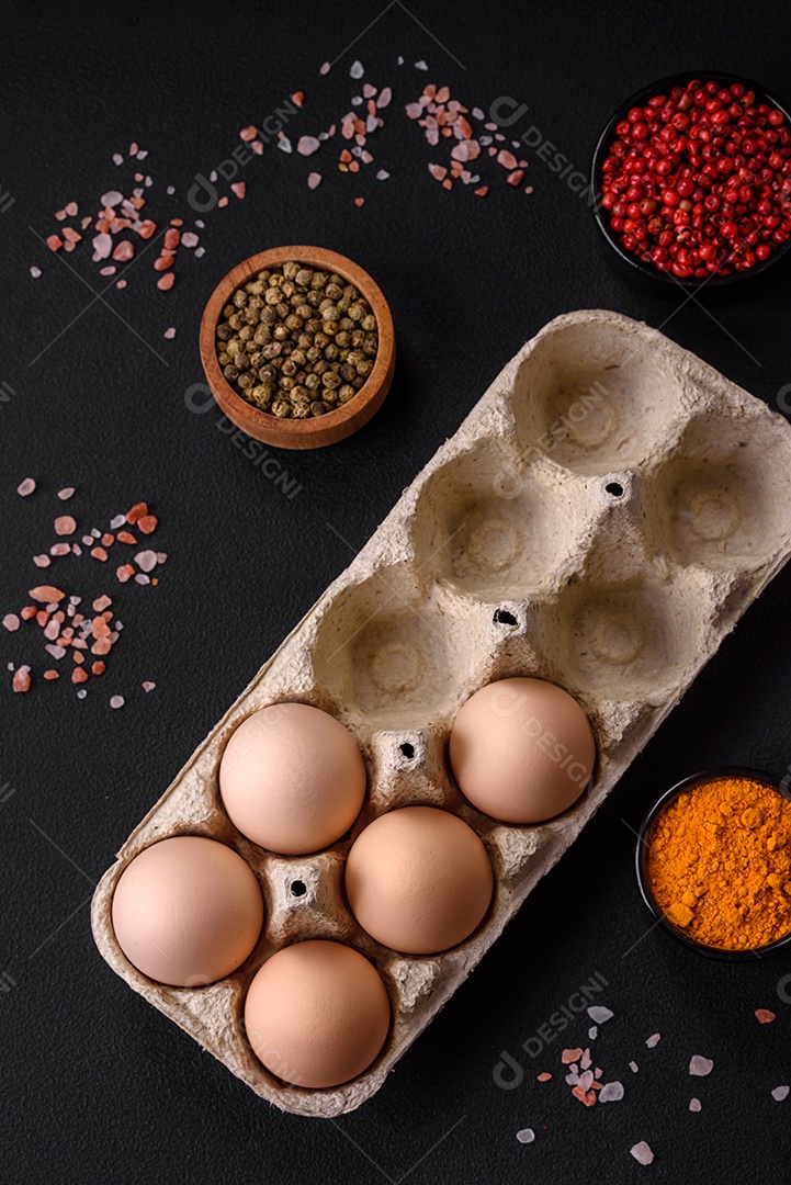 Ovos de galinha crus frescos na cor bege em uma bandeja de papelão sobre um fundo escuro de concreto