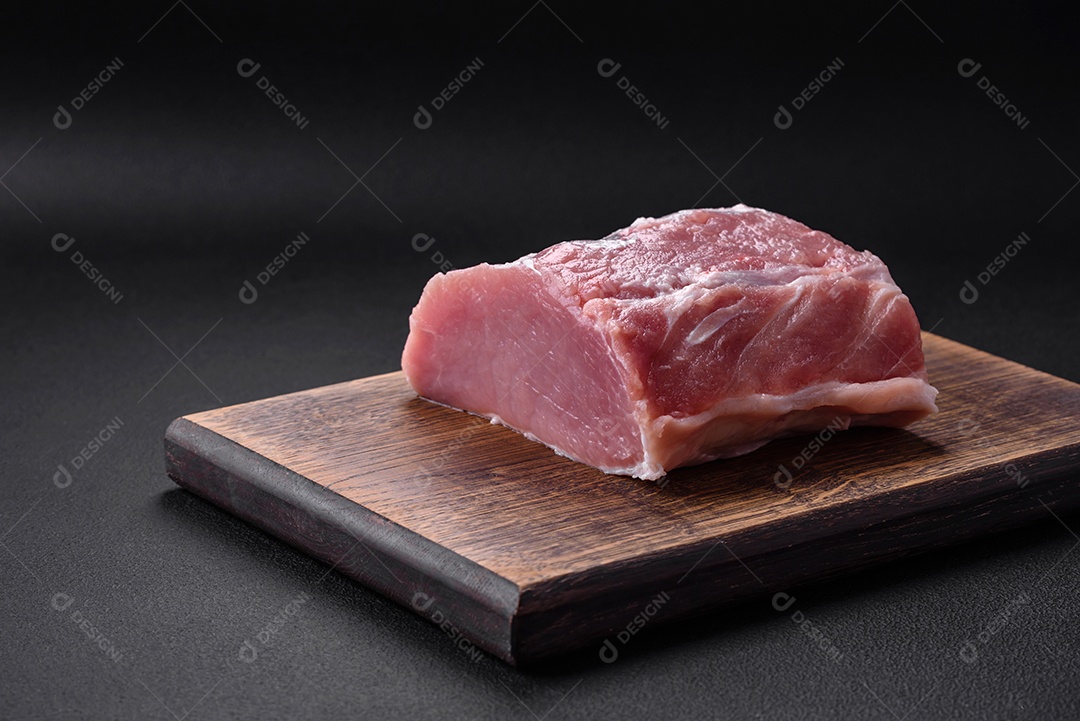 Carne de porco fresca e suculenta sobre uma tábua de madeira com especiarias e sal sobre um fundo escuro de concreto