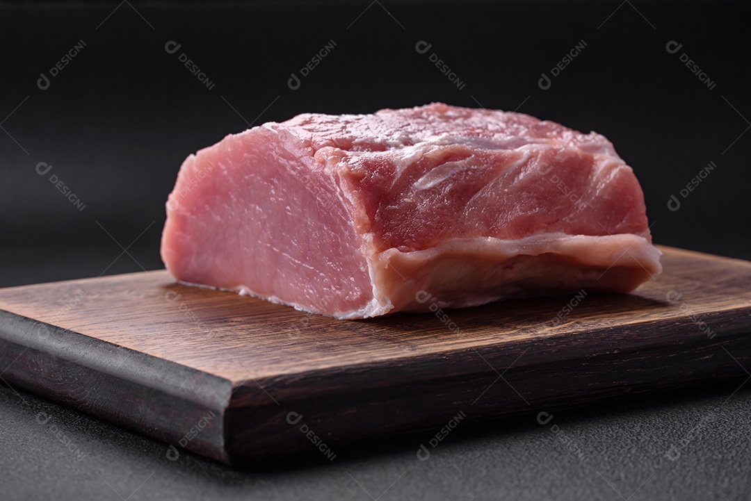 Carne de porco fresca e suculenta sobre uma tábua de madeira com especiarias e sal sobre um fundo escuro de concreto
