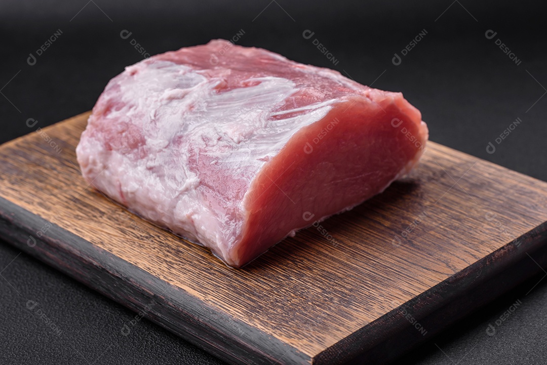 Carne de porco fresca e suculenta sobre uma tábua de madeira com especiarias e sal sobre um fundo escuro de concreto