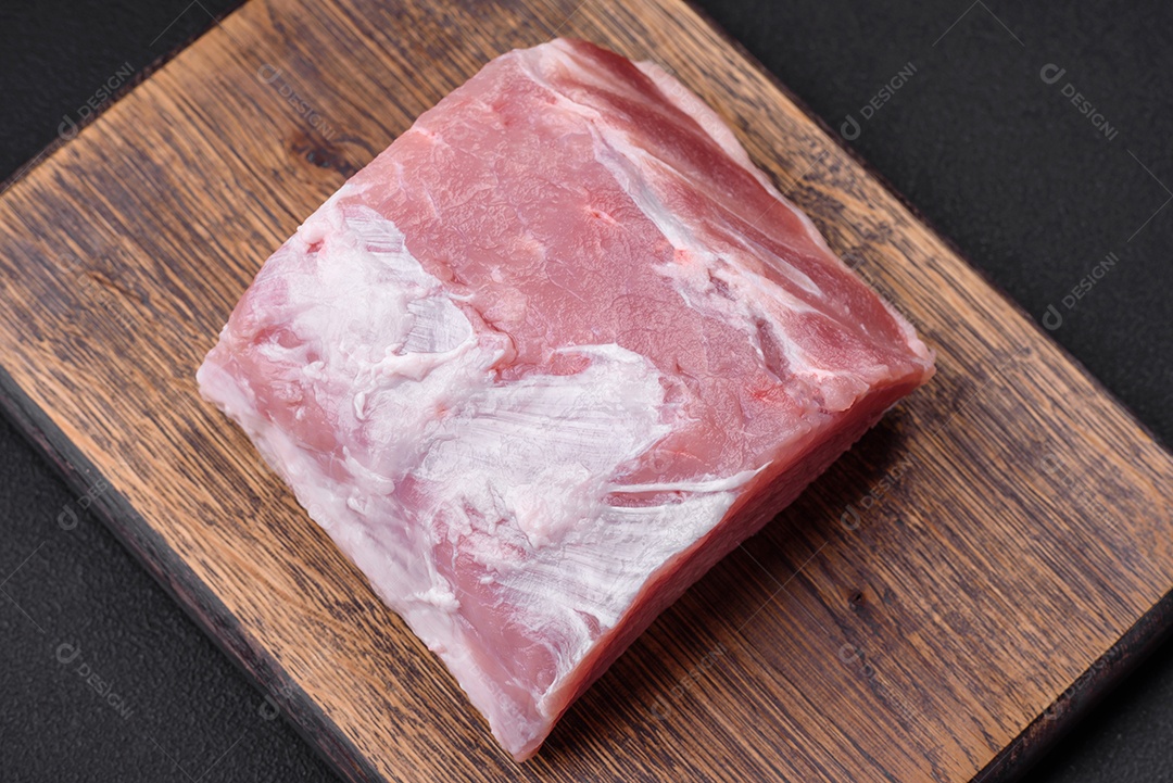 Carne de porco fresca e suculenta sobre uma tábua de madeira com especiarias e sal sobre um fundo escuro de concreto