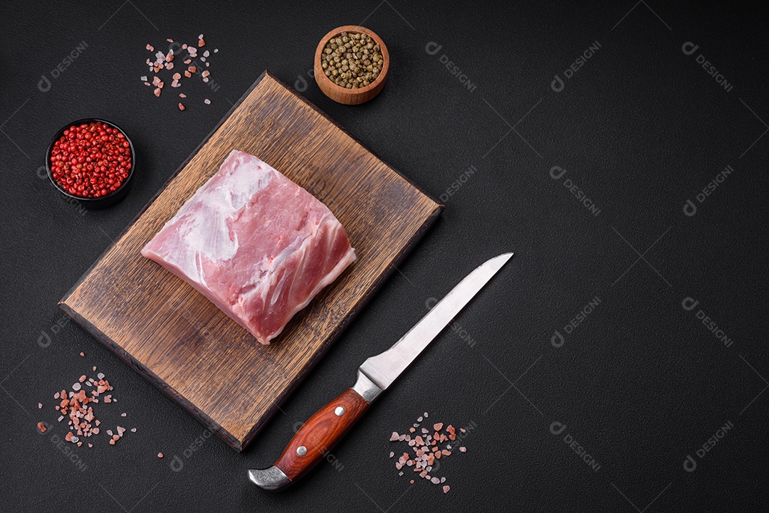 Carne de porco fresca e suculenta sobre uma tábua de madeira com especiarias e sal sobre um fundo escuro de concreto