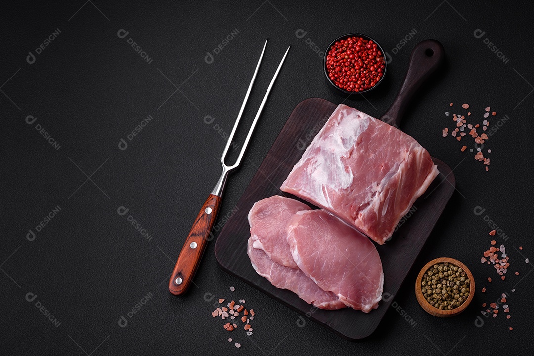 Carne de porco fresca e suculenta sobre uma tábua de madeira com especiarias e sal sobre um fundo escuro de concreto