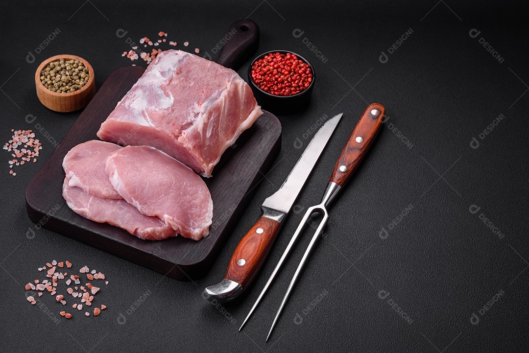 Carne de porco fresca e suculenta sobre uma tábua de madeira com especiarias e sal sobre um fundo escuro de concreto
