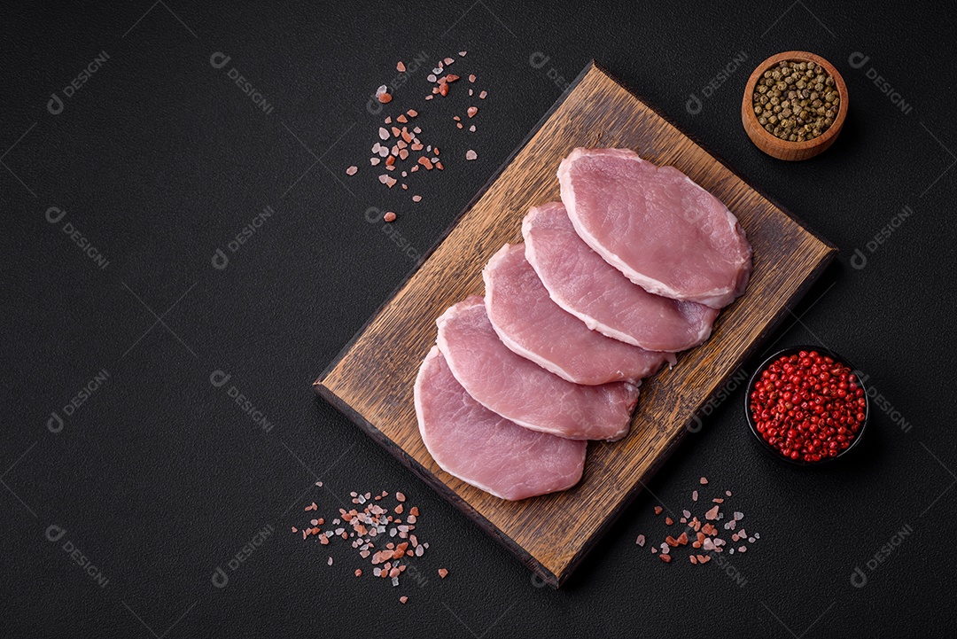 Carne de porco fresca e suculenta sobre uma tábua de madeira com especiarias e sal sobre um fundo escuro de concreto