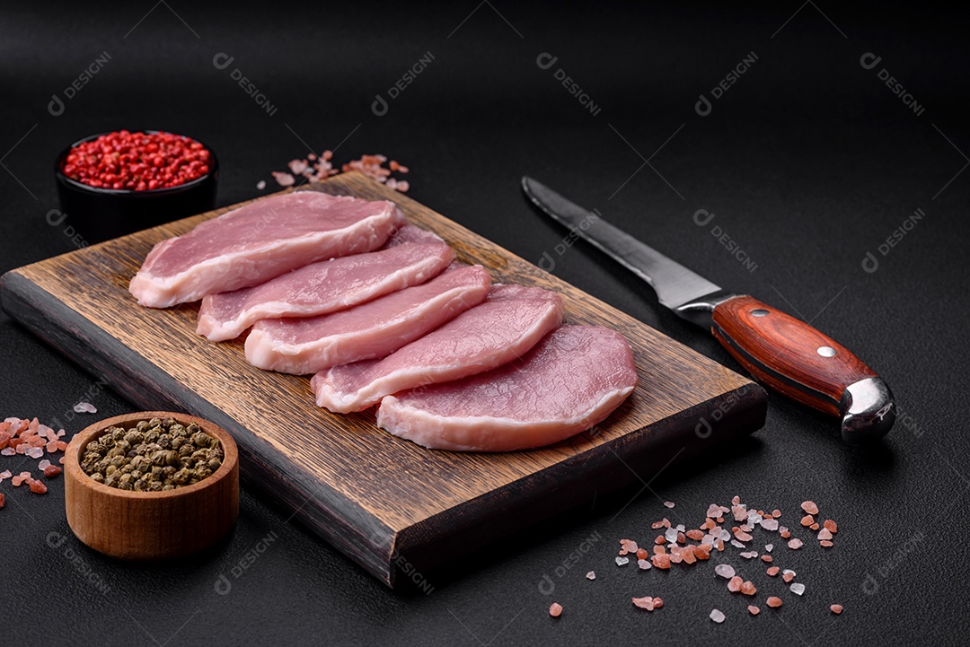 Carne de porco fresca e suculenta sobre uma tábua de madeira com especiarias e sal sobre um fundo escuro de concreto