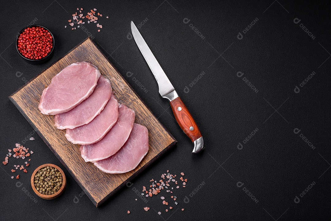 Carne de porco fresca e suculenta sobre uma tábua de madeira com especiarias e sal sobre um fundo escuro de concreto