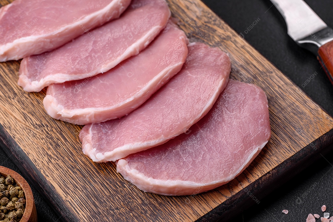 Carne de porco fresca e suculenta sobre uma tábua de madeira com especiarias e sal sobre um fundo escuro de concreto