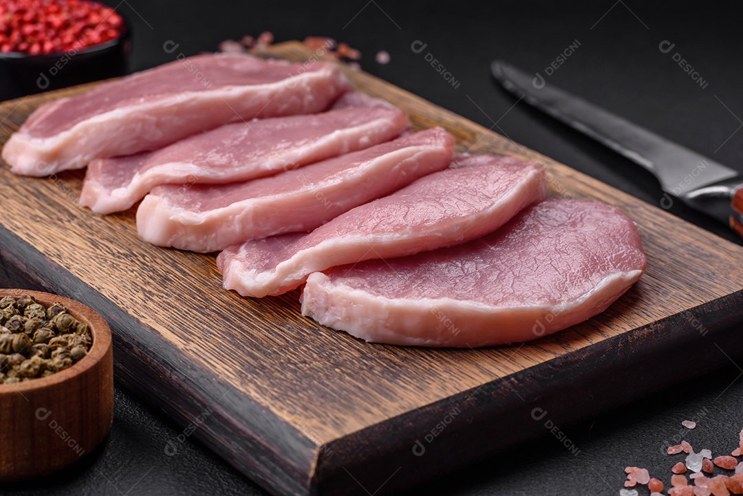 Carne de porco fresca e suculenta sobre uma tábua de madeira com especiarias e sal sobre um fundo escuro de concreto