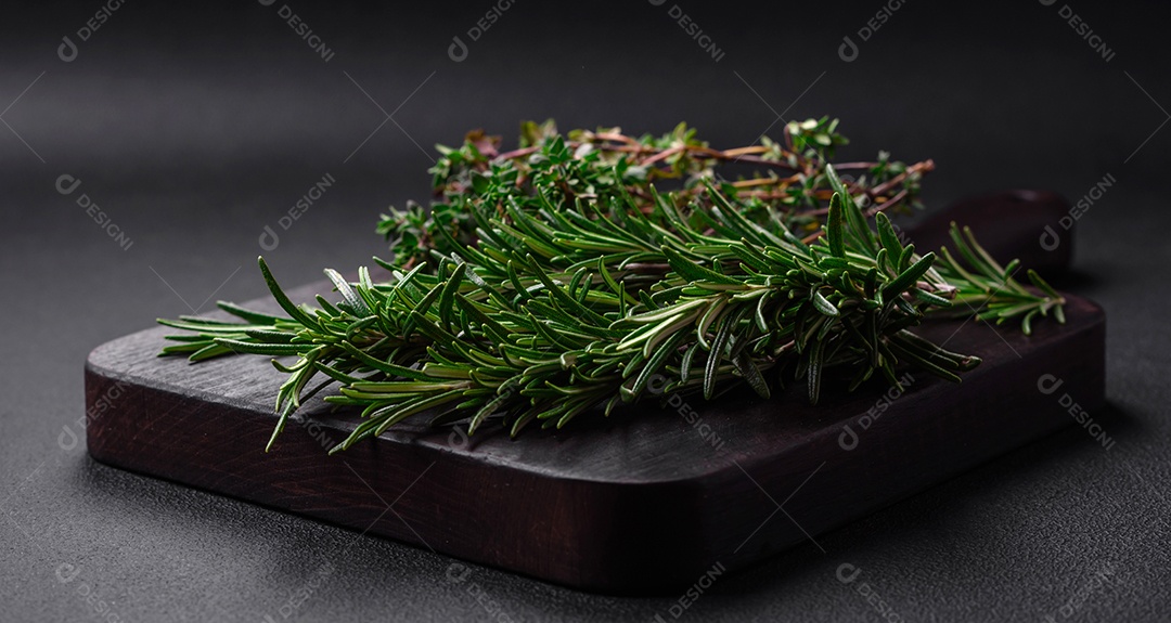 Raminhos de alecrim verde fresco sobre uma tábua de madeira sobre um fundo escuro de concreto