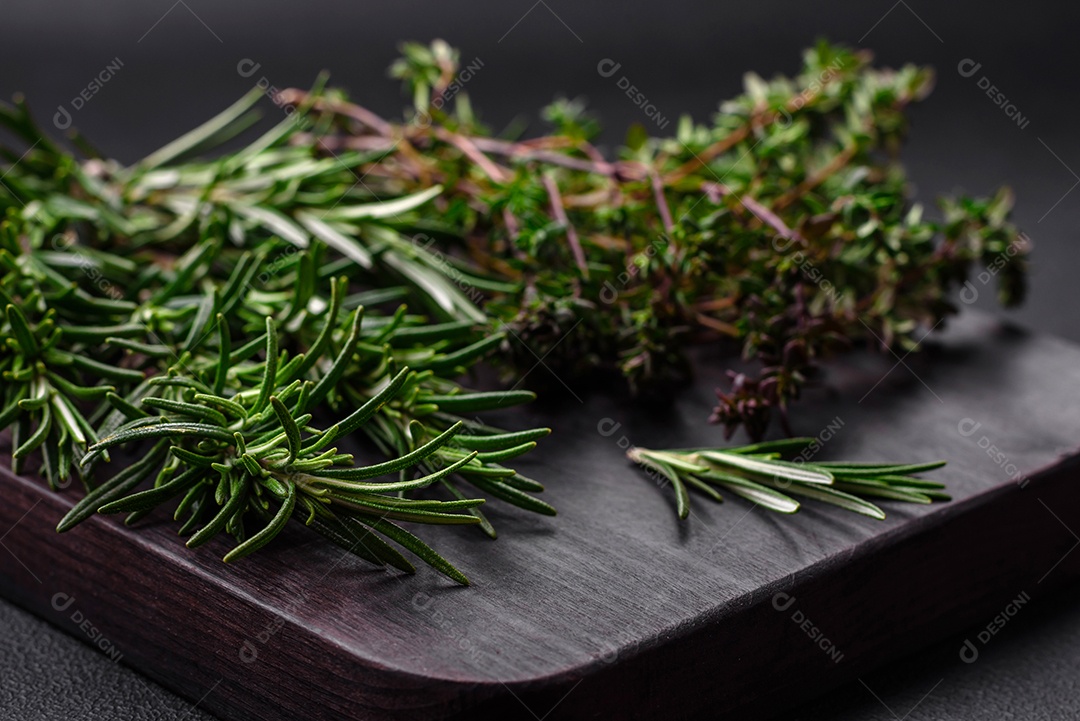 Raminhos de alecrim verde fresco sobre uma tábua de madeira sobre um fundo escuro de concreto