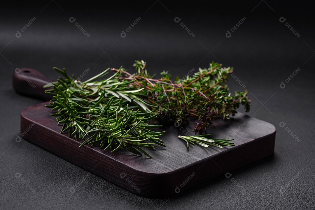 Raminhos de alecrim verde fresco sobre uma tábua de madeira sobre um fundo escuro de concreto