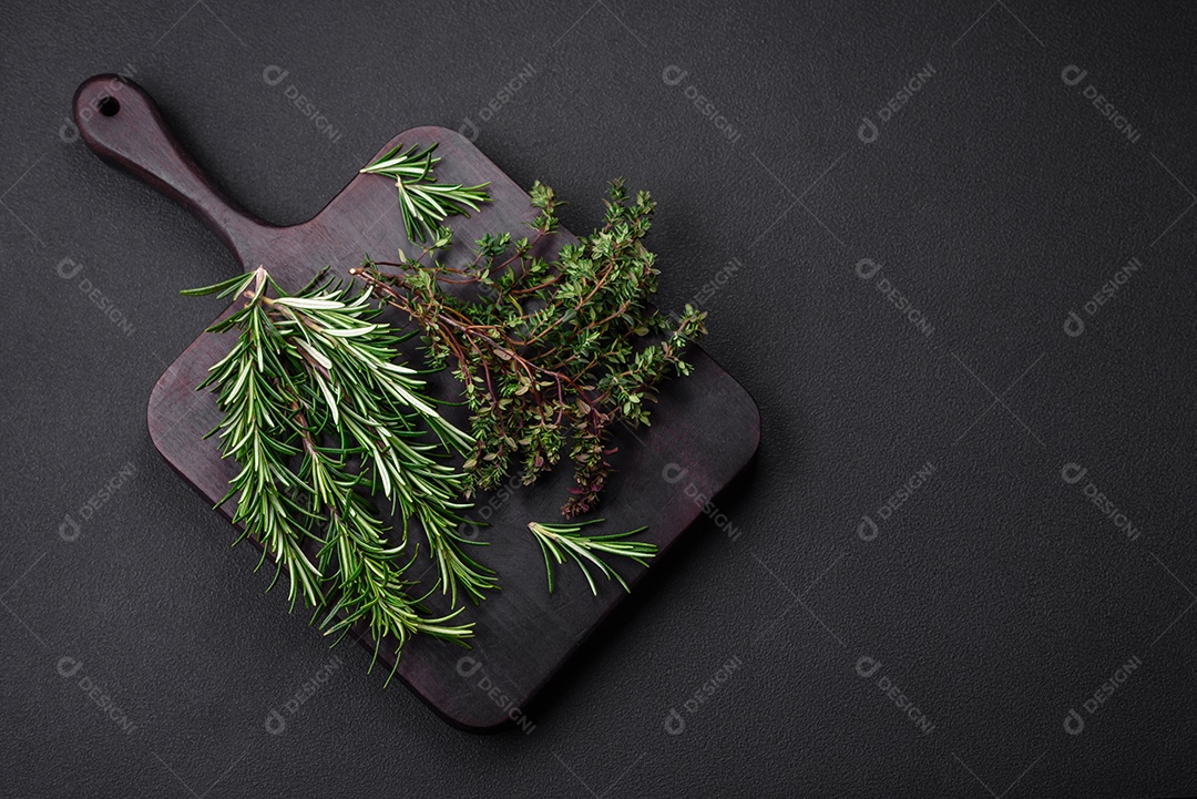 Raminhos de alecrim verde fresco sobre uma tábua de madeira sobre um fundo escuro de concreto