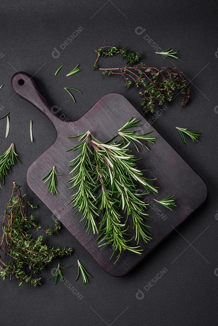 Raminhos de alecrim verde fresco sobre uma tábua de madeira sobre um fundo escuro de concreto