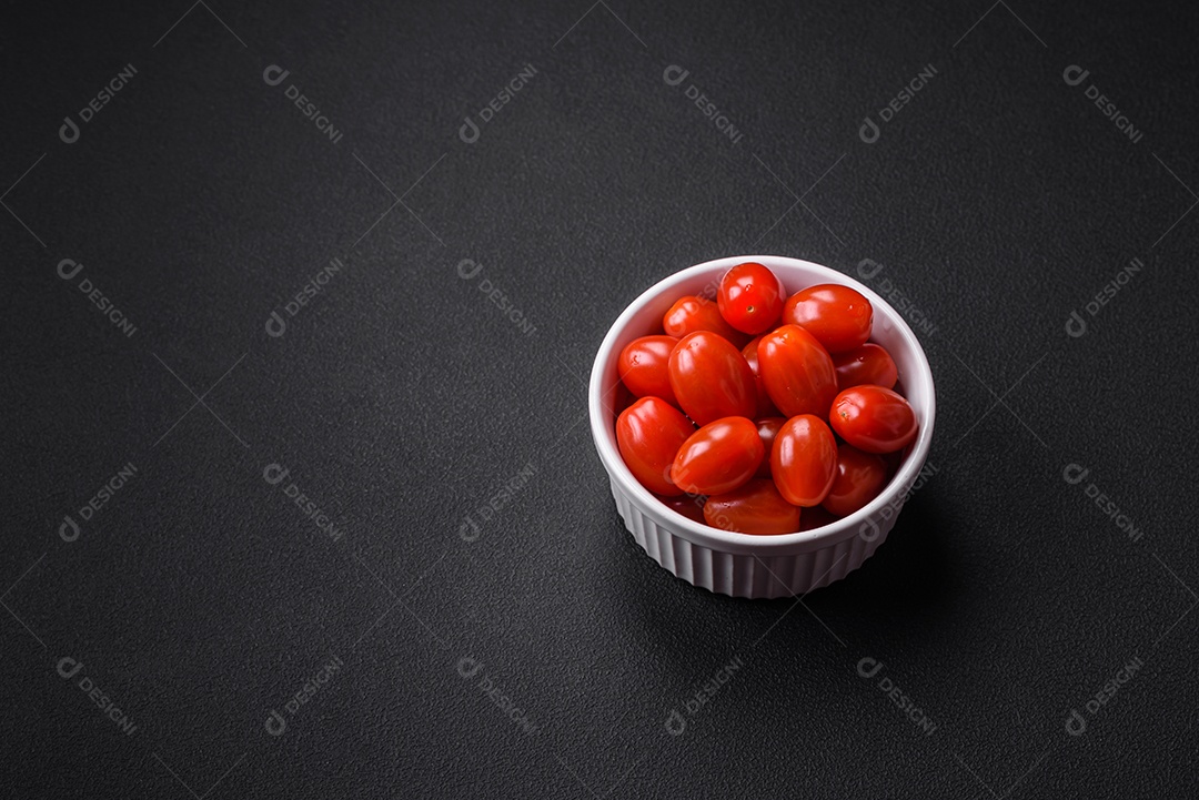 Tomates cereja frescos e saborosos em uma tigela branca com nervuras sobre um fundo escuro de concreto