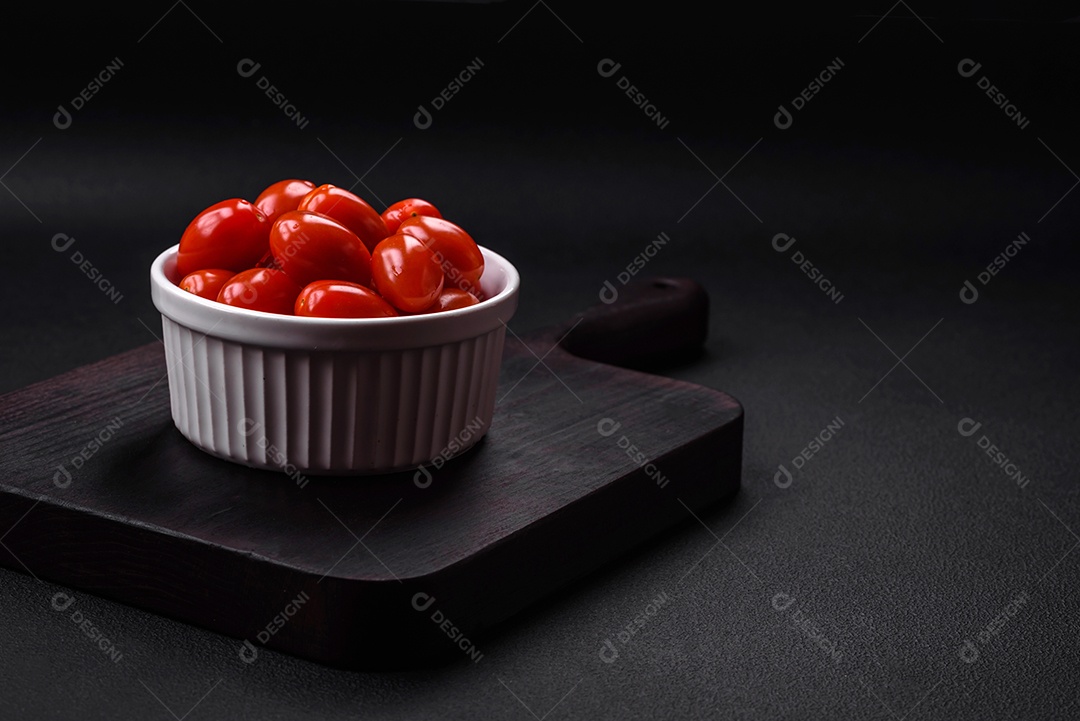 Tomates cereja frescos e saborosos em uma tigela branca com nervuras sobre um fundo escuro de concreto