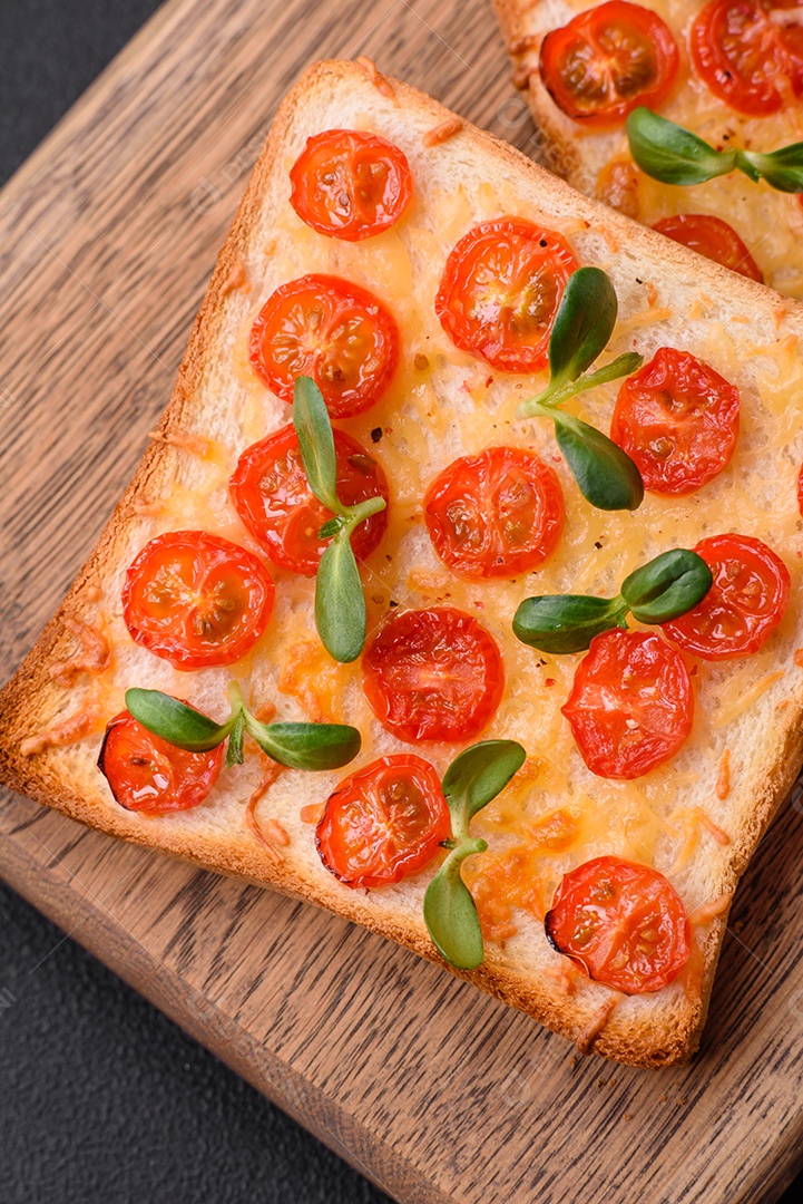 Deliciosa torrada fresca ou bruschetta com tomate, queijo, ervas, sal e especiarias sobre fundo escuro de concreto
