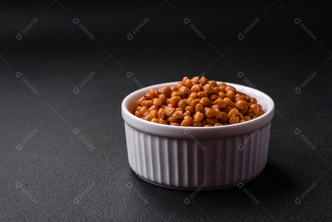 Deliciosas lentilhas enlatadas saudáveis ​​em uma tigela branca com nervuras de cerâmica sobre um fundo escuro de concreto