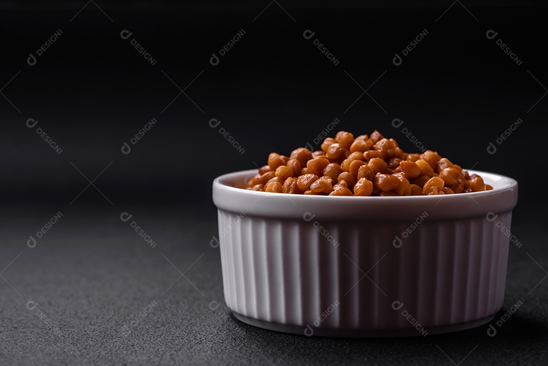 Deliciosas lentilhas enlatadas saudáveis ​​em uma tigela branca com nervuras de cerâmica sobre um fundo escuro de concreto