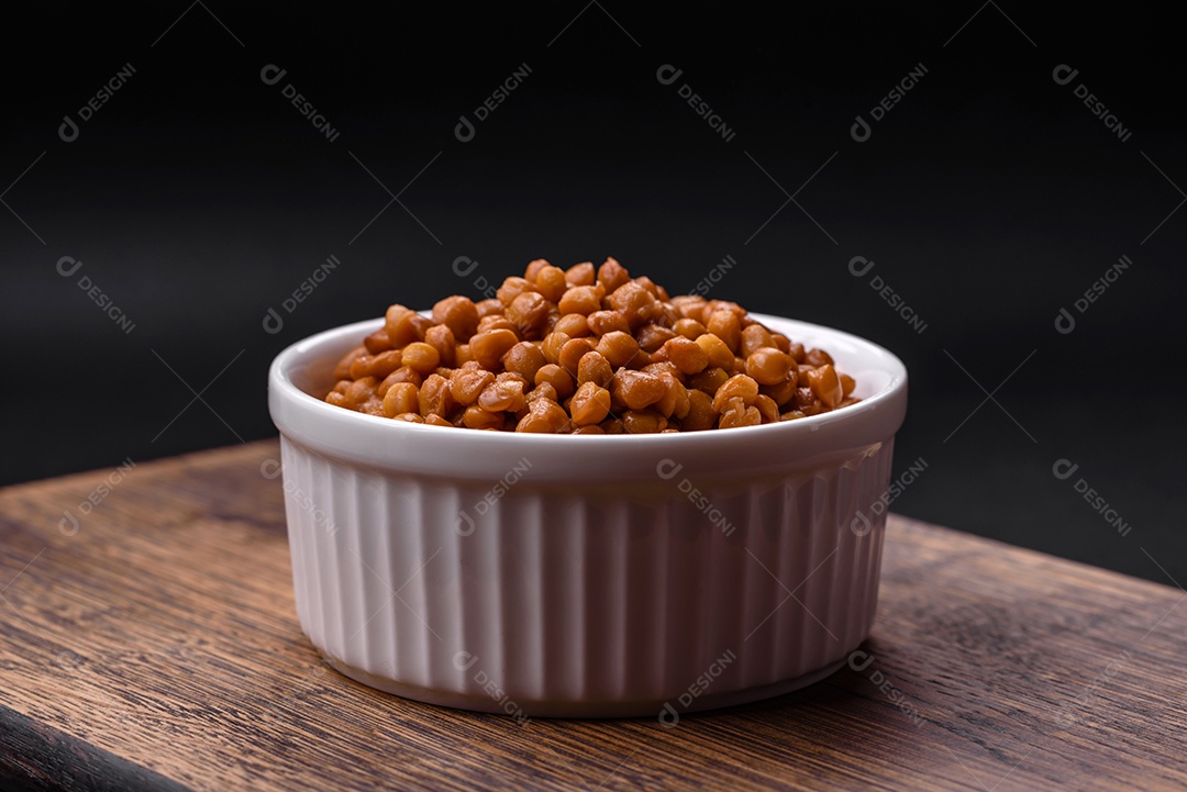 Deliciosas lentilhas enlatadas saudáveis ​​em uma tigela branca com nervuras de cerâmica sobre um fundo escuro de concreto
