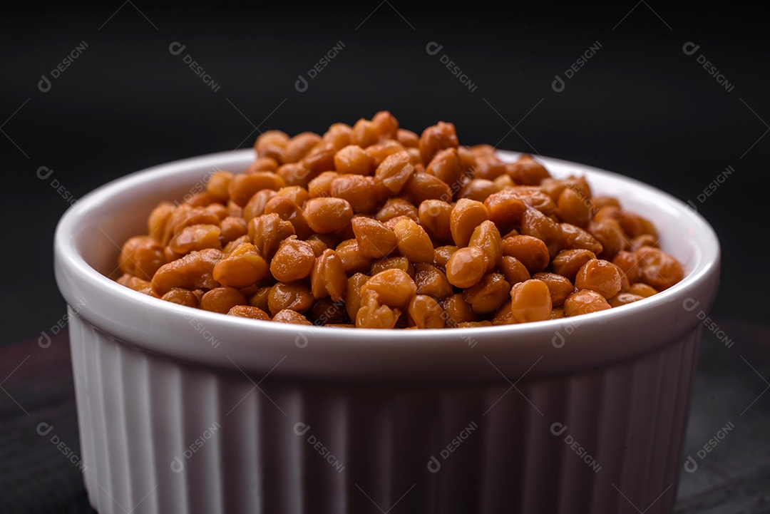 Deliciosas lentilhas enlatadas saudáveis ​​em uma tigela branca com nervuras de cerâmica sobre um fundo escuro de concreto