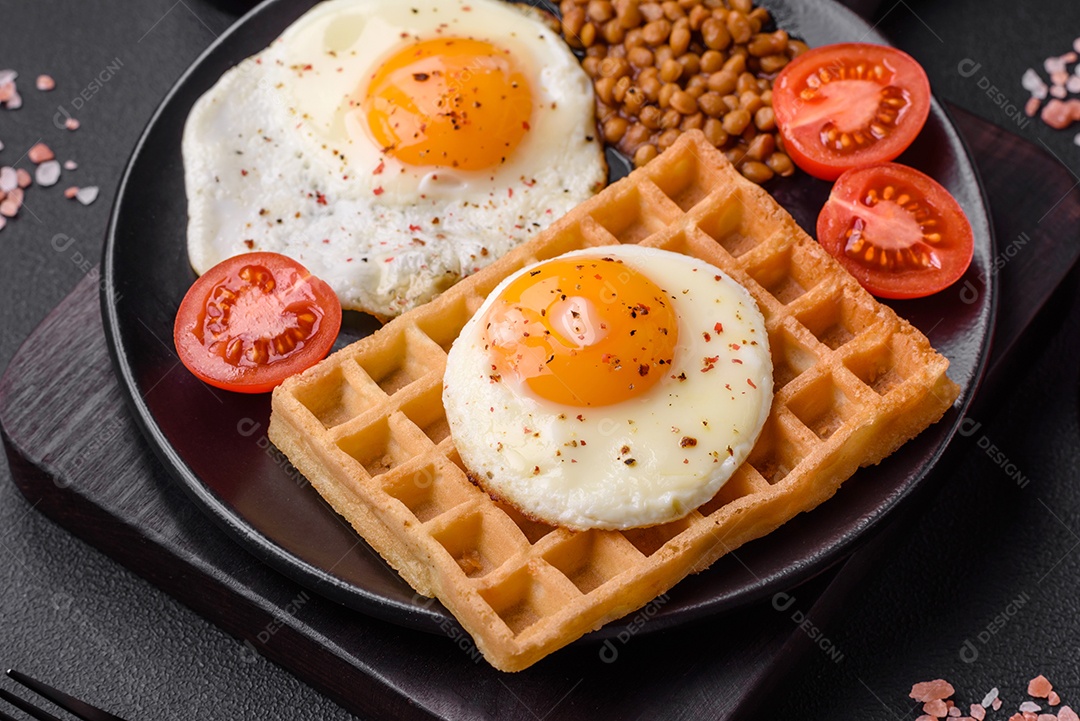 Delicioso café da manhã composto por ovo frito, waffle belga, lentilhas, microgreens com especiarias e ervas em um fundo escuro de concreto