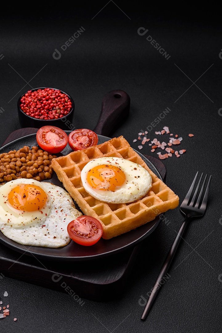Delicioso café da manhã composto por ovo frito, waffle belga, lentilhas, microgreens com especiarias e ervas em um fundo escuro de concreto