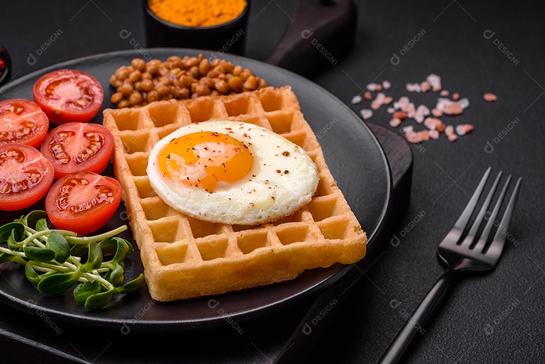 Delicioso café da manhã composto por ovo frito, waffle belga, lentilhas, microgreens com especiarias e ervas em um fundo escuro de concreto