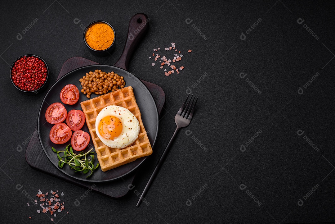 Delicioso café da manhã composto por ovo frito, waffle belga, lentilhas, microgreens com especiarias e ervas em um fundo escuro de concreto