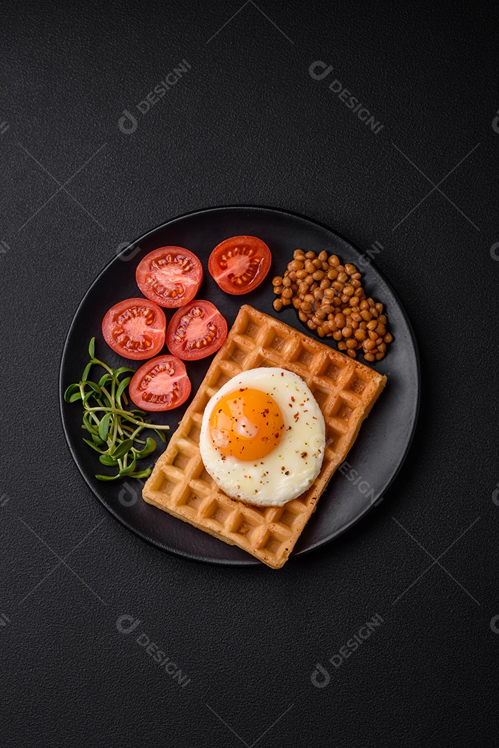 Delicioso café da manhã composto por ovo frito, waffle belga, lentilhas, microgreens com especiarias e ervas em um fundo escuro de concreto