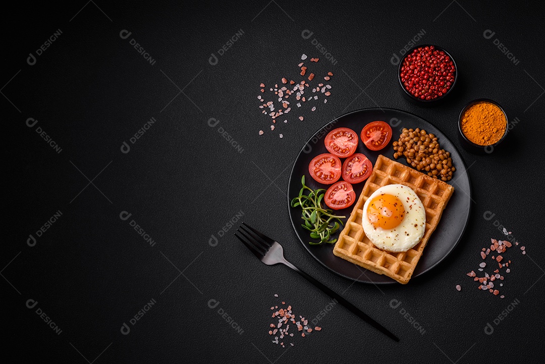 Delicioso café da manhã composto por ovo frito, waffle belga, lentilhas, microgreens com especiarias e ervas em um fundo escuro de concreto