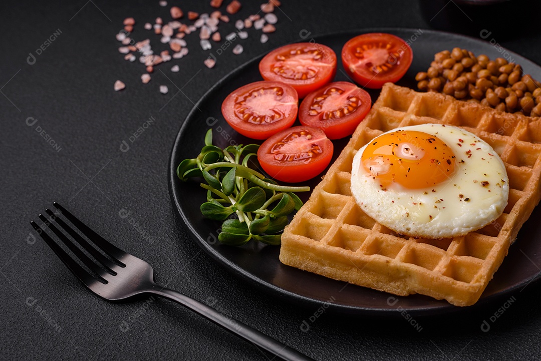 Delicioso café da manhã composto por ovo frito, waffle belga, lentilhas, microgreens com especiarias e ervas em um fundo escuro de concreto