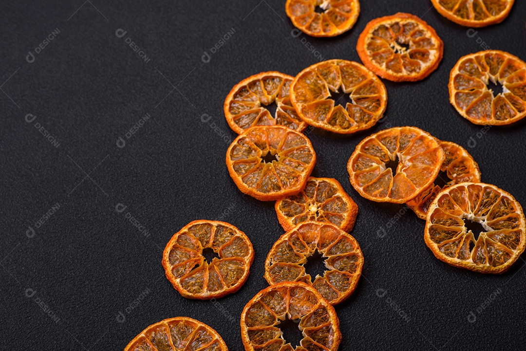 Fatias secas de forma redonda de tangerina de cor laranja brilhante sobre um fundo textural escuro