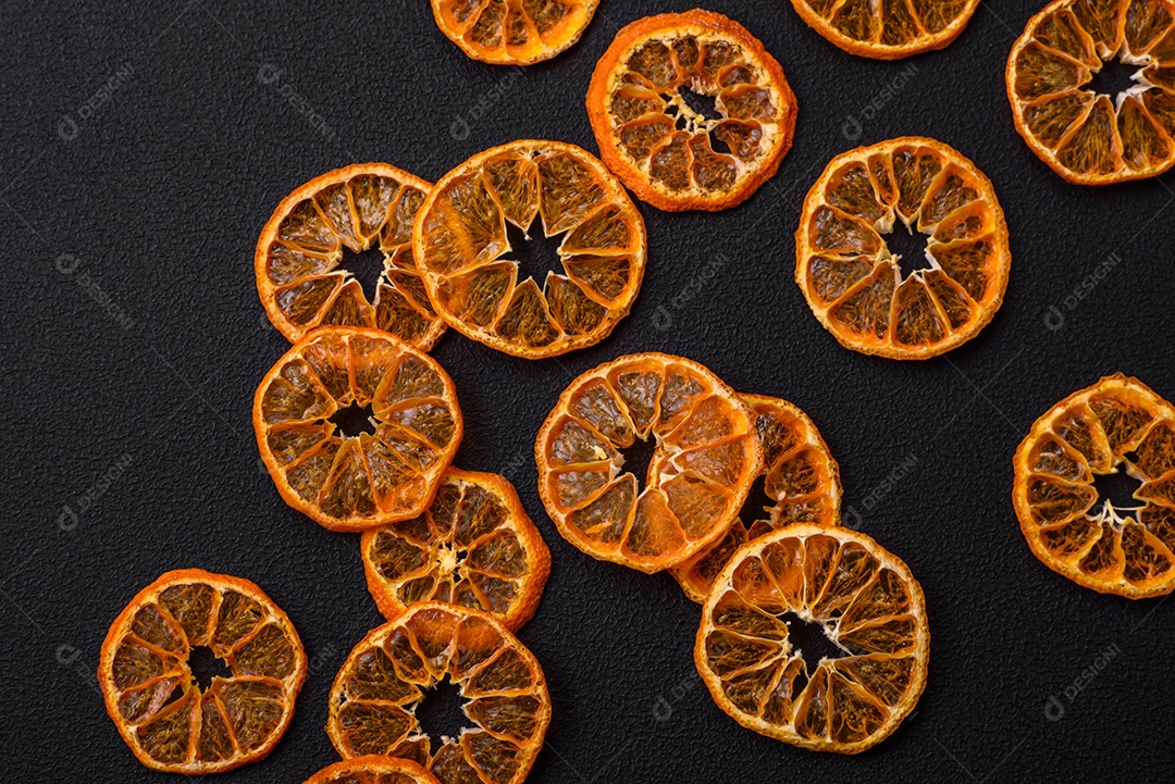 Fatias secas de forma redonda de tangerina de cor laranja brilhante sobre um fundo textural escuro