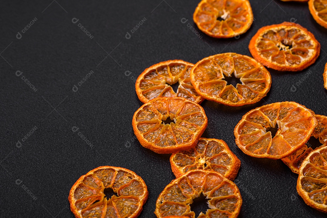 Fatias secas de forma redonda de tangerina de cor laranja brilhante sobre um fundo textural escuro