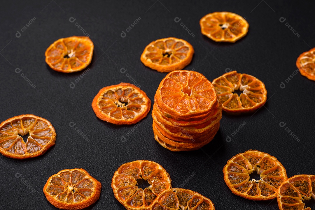 Fatias secas de forma redonda de tangerina de cor laranja brilhante sobre um fundo textural escuro