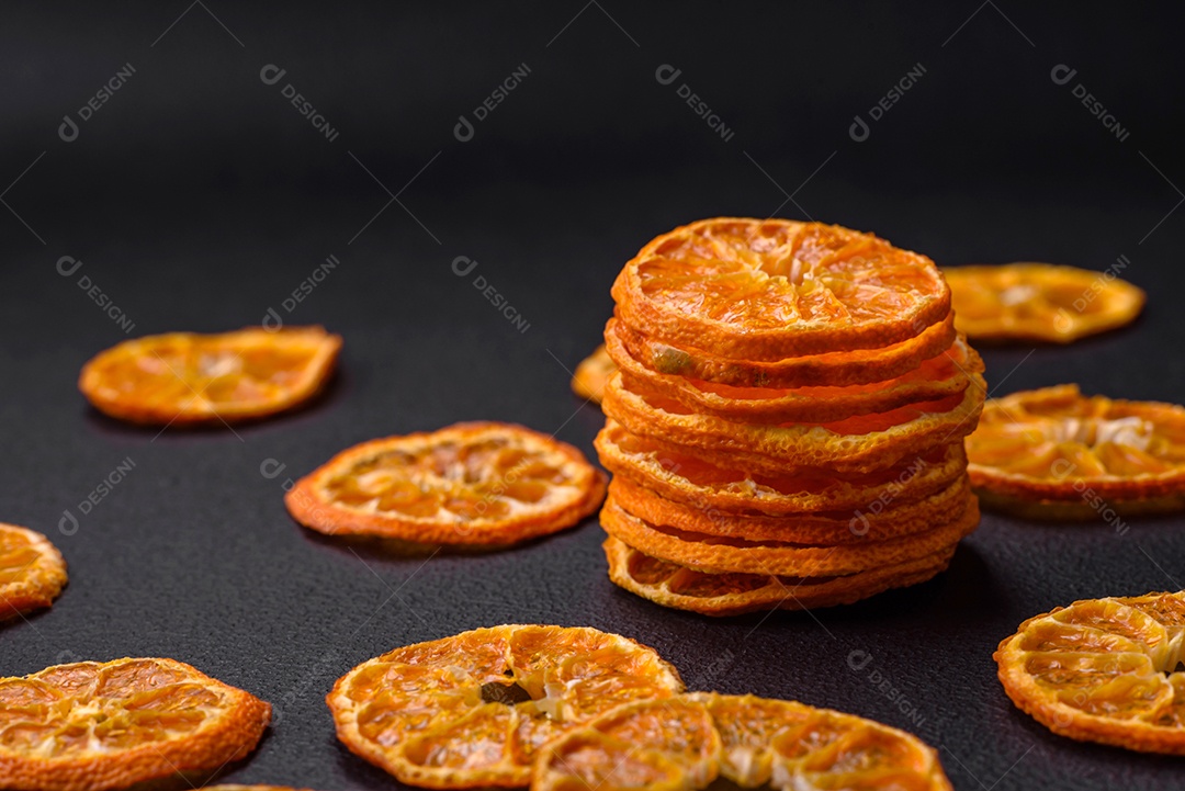 Fatias secas de forma redonda de tangerina de cor laranja brilhante sobre um fundo textural escuro