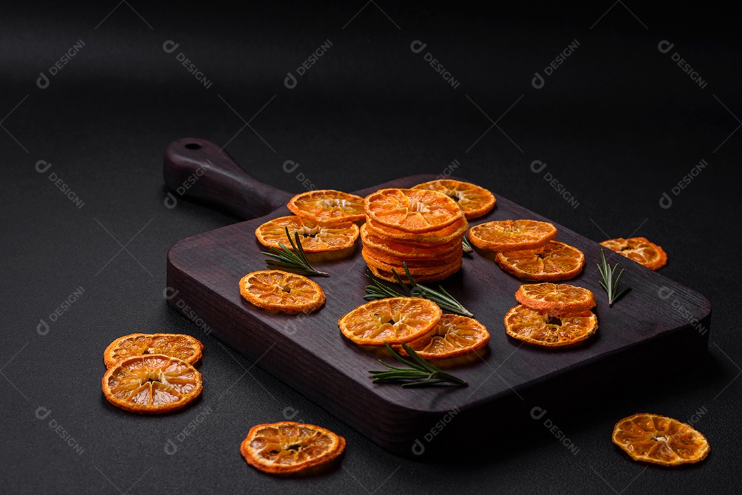 Fatias secas de forma redonda de tangerina de cor laranja brilhante sobre um fundo textural escuro