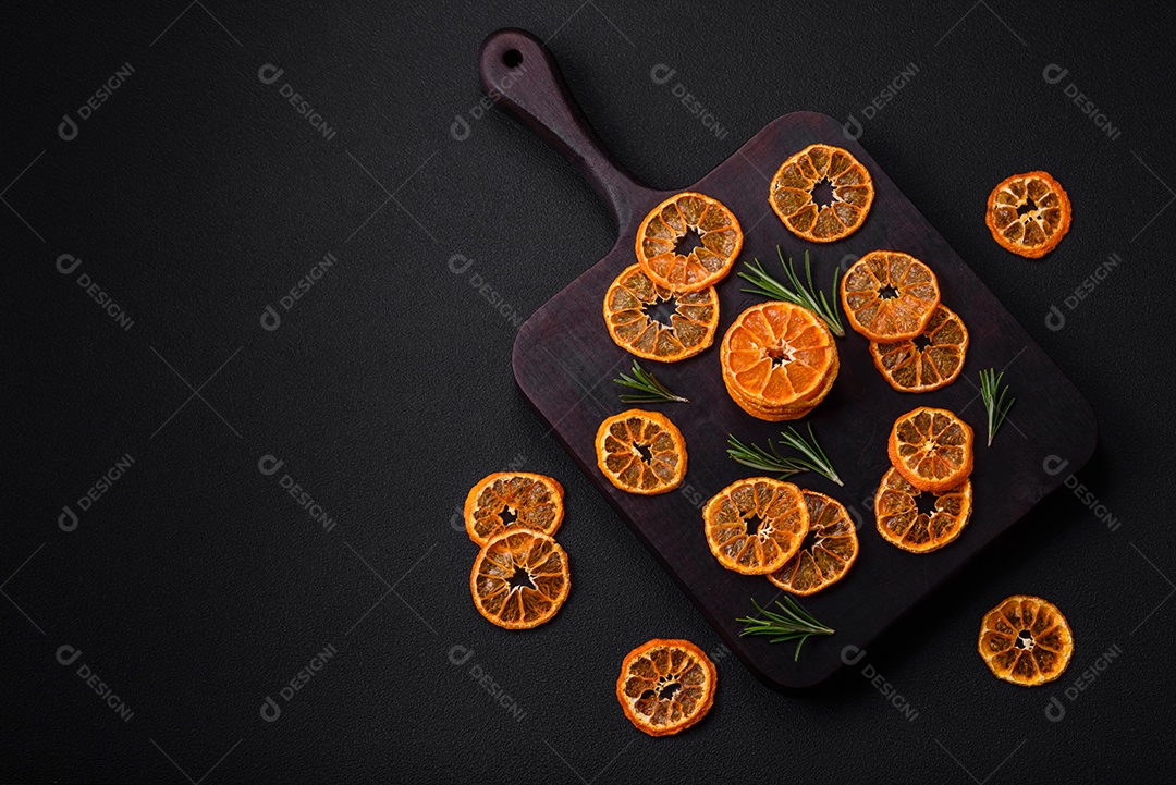 Fatias secas de forma redonda de tangerina de cor laranja brilhante sobre um fundo textural escuro