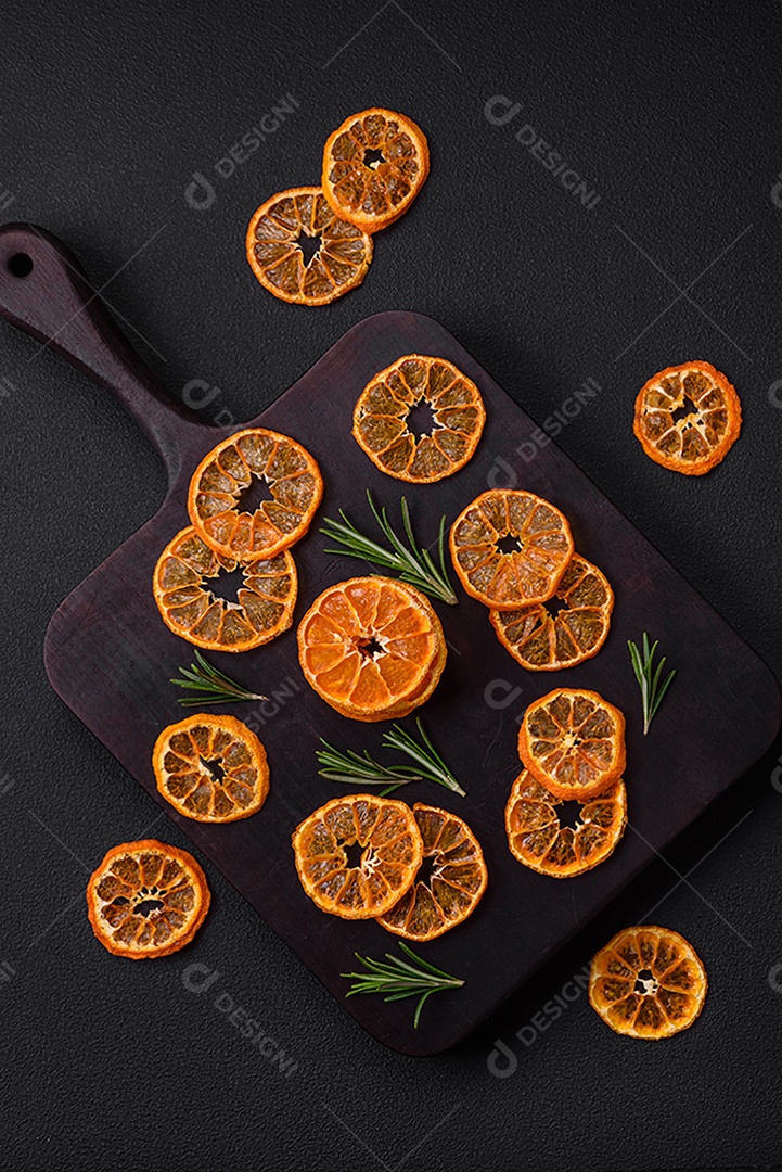 Fatias secas de forma redonda de tangerina de cor laranja brilhante sobre um fundo textural escuro