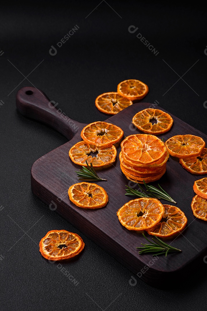 Fatias secas de forma redonda de tangerina de cor laranja brilhante sobre um fundo textural escuro