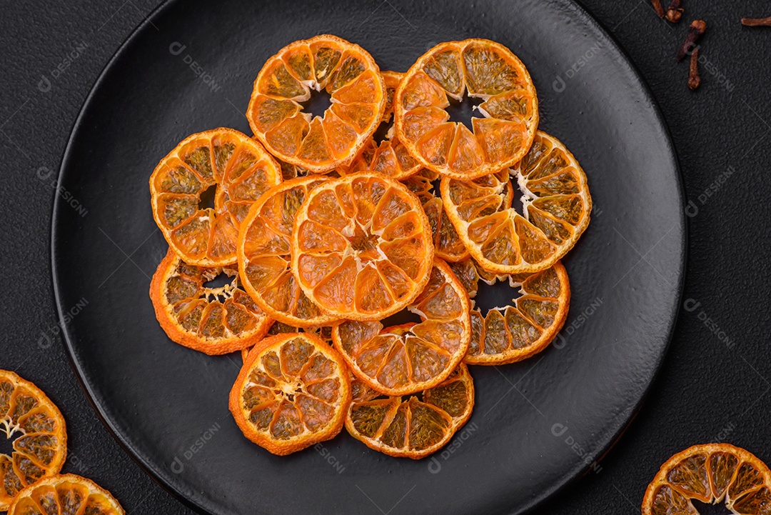 Fatias secas de forma redonda de tangerina de cor laranja brilhante sobre um fundo textural escuro